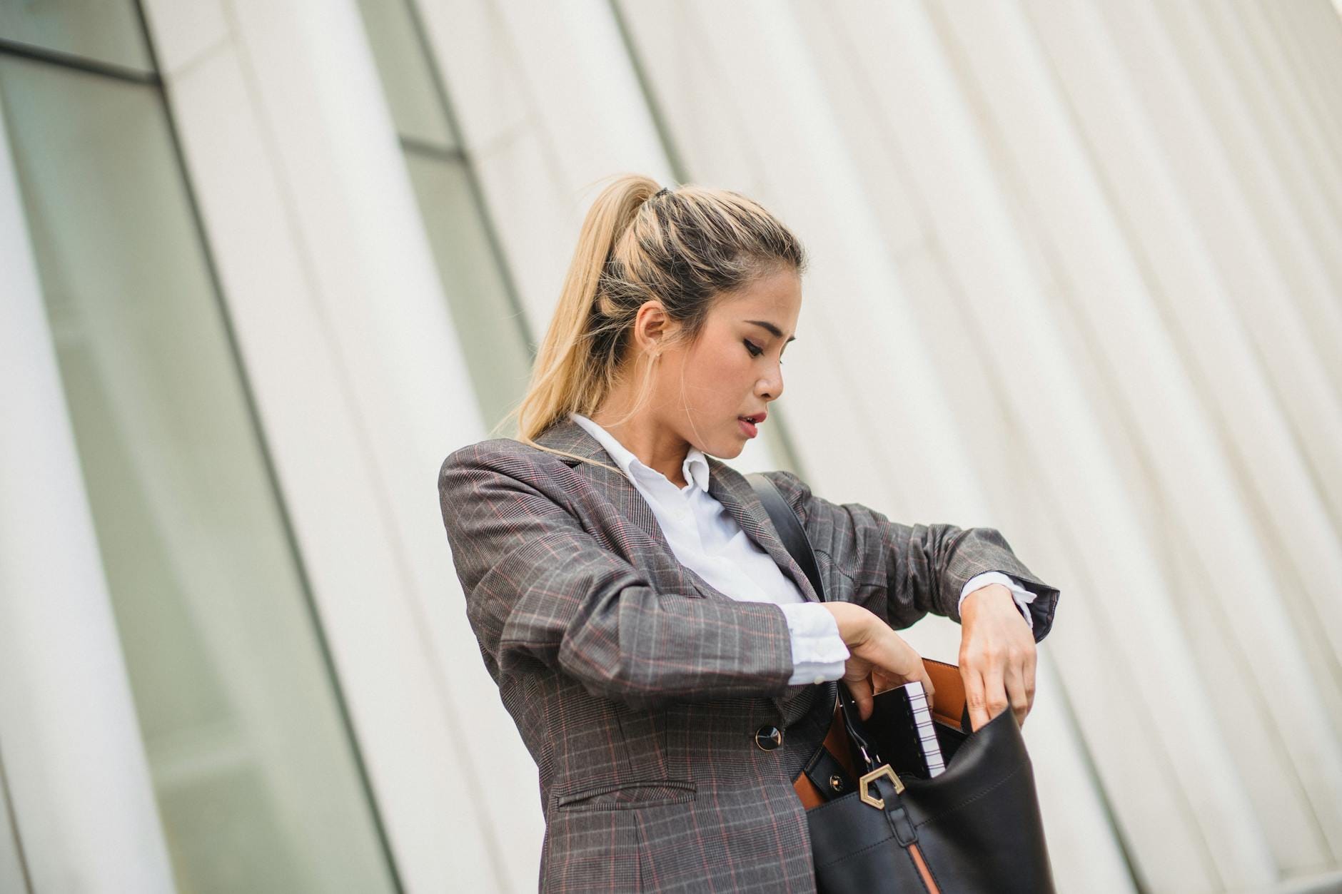 Elegancka kobieta w marynarce sprawdza zawartość torebki na ulicy