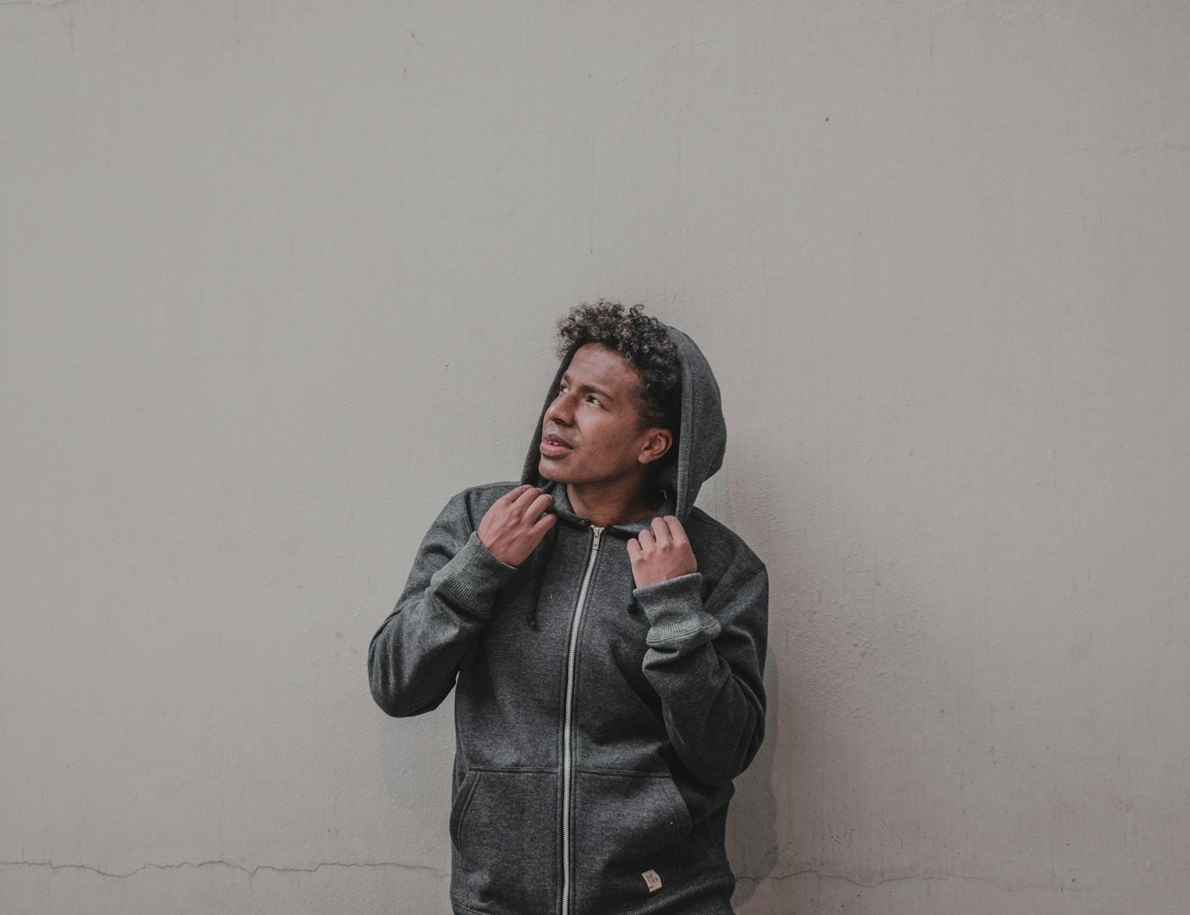 Mężczyzna w szarej bluzie i kurtce patrzy w górę na neutralnym tle
