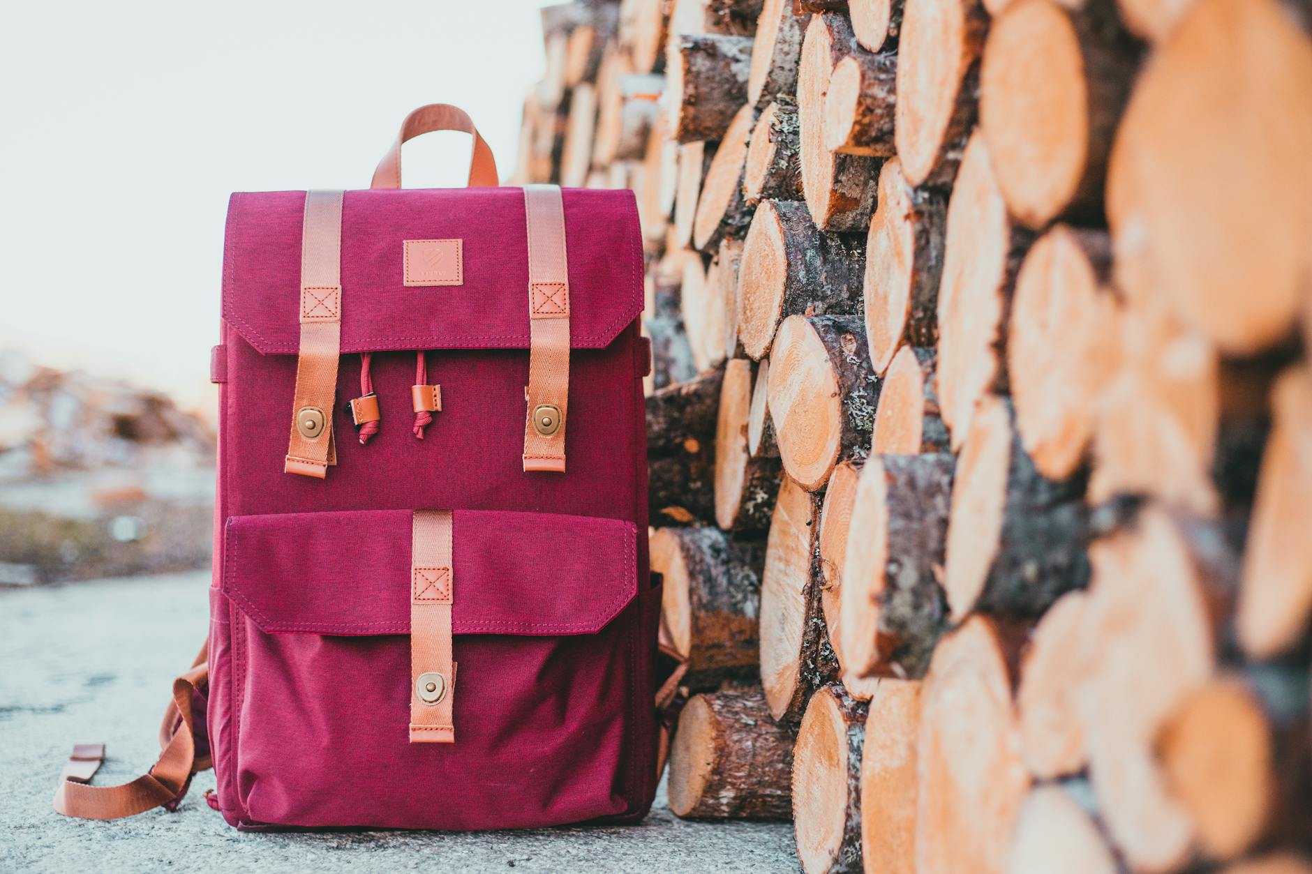 Jak mądrze kupować torby i plecaki aby stworzyć funkcjonalną bazę dodatków Bordowy plecak z paskami skórzanymi na tle stosu drewnianych bali