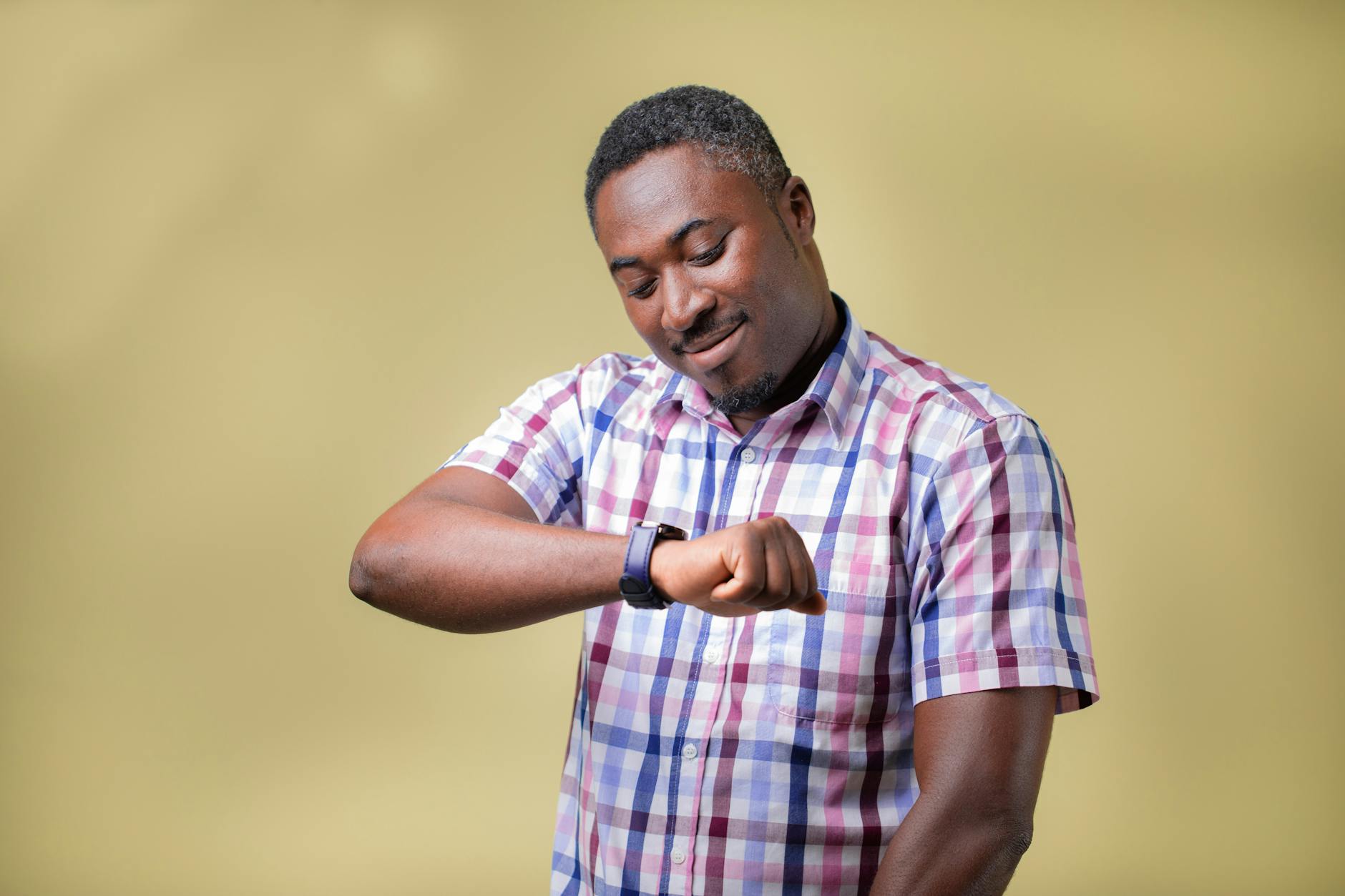 Mężczyzna w casualowym stroju sprawdza zegarek na tle żółtej ściany