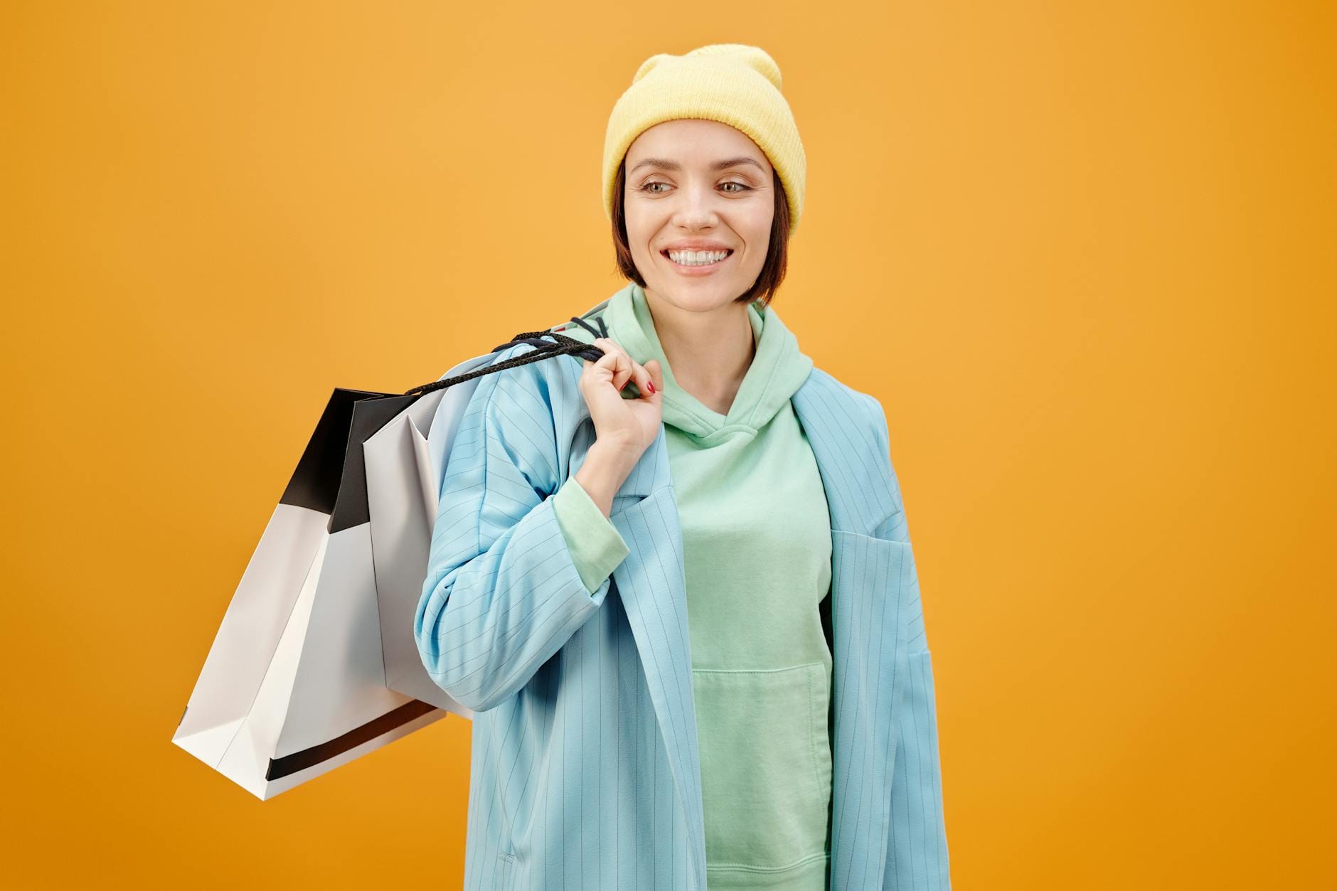 Uśmiechnięta kobieta w casualowej stylizacji z torbą shopper na żółtym tle
