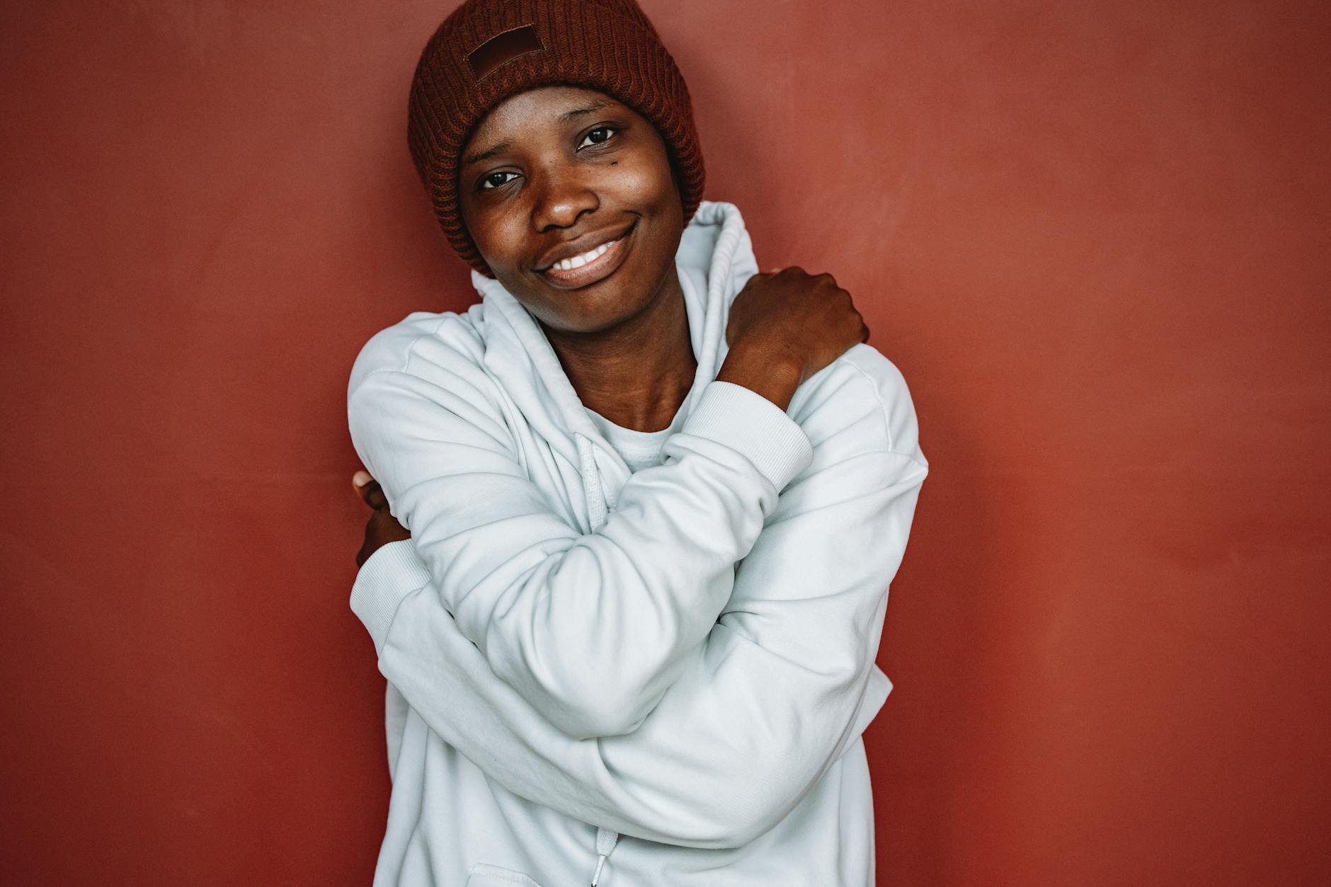 Uśmiechnięta kobieta w kolorowej bluzie i czapce na czerwonym tle