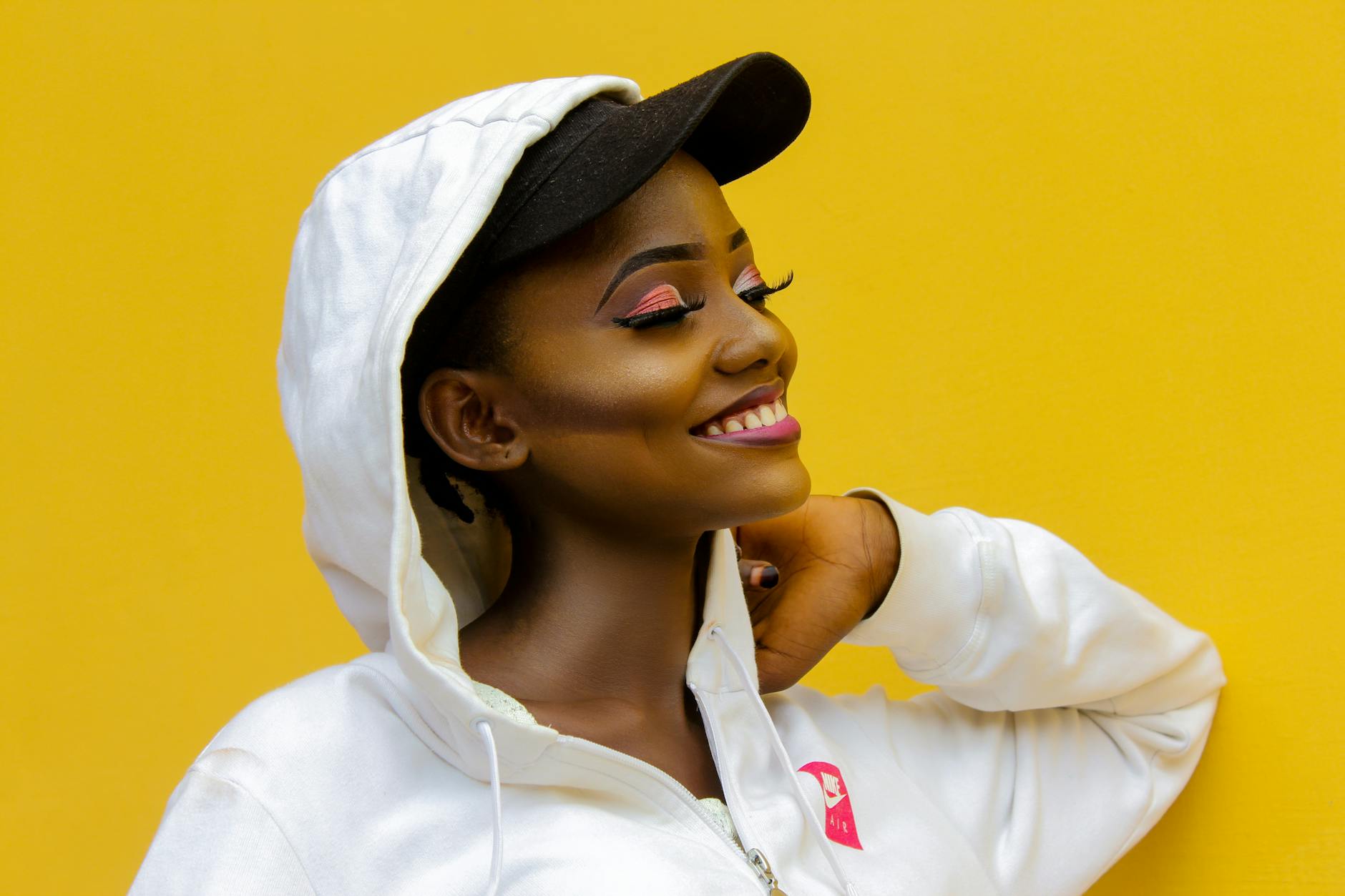 Stylizacje z bluzami w intensywnych kolorach: jak je tonować dodatkami Uśmiechnięta kobieta w kolorowej bluzie i czapce na żółtym tle