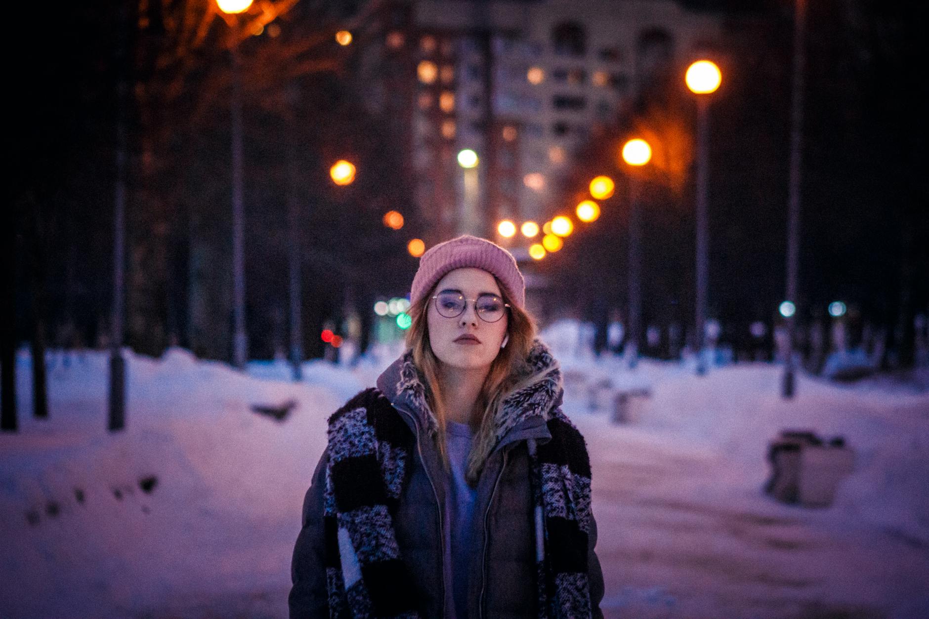 Kobieta w zimowej kurtce idzie wieczorem przez oświetlony, zaśnieżony park