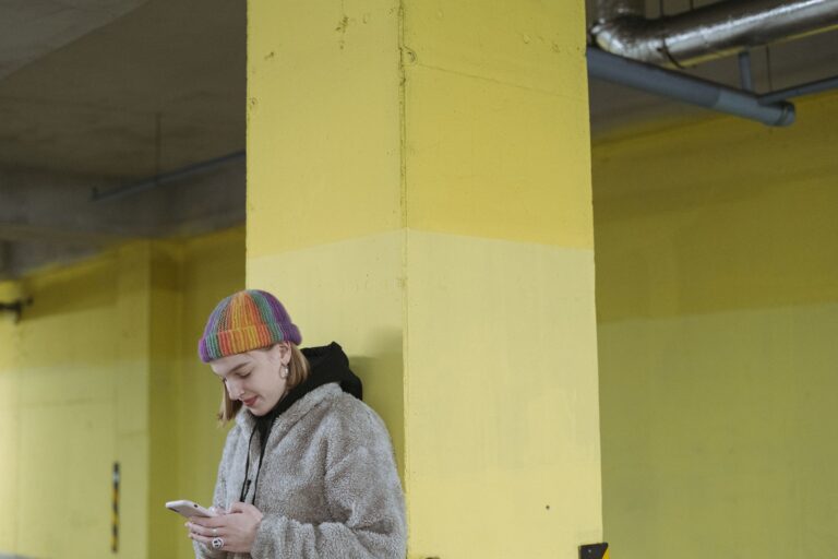 Kobieta oparta o żółty słup korzysta ze smartfona w mieście